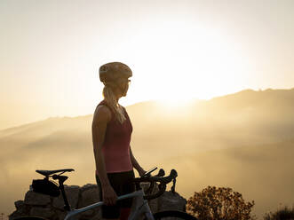 Sportlerin mit Helm schaut in den Sonnenuntergang - MALF00382