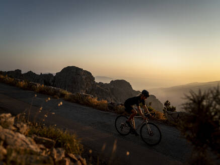 Athlete cycling on mountain road at sunset - MALF00386