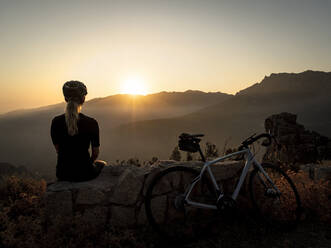 Sportlerin sitzt auf einem Felsen und betrachtet den Sonnenuntergang - MALF00387