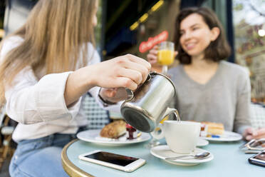 Junge Frau gießt Kaffee in eine Tasse für einen Freund in einem Café - WPEF05507