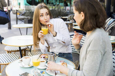 Aufgeregte Frau, die einen Saft trinkt und einen Freund ansieht, der im Cafe gestikuliert - WPEF05509