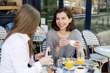 Junge Frau unterhält sich mit einem Freund und buttert Baguette im Café - WPEF05513