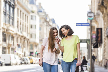 Lächelnde junge Frau zeigt Handy mit Freund auf der Straße - WPEF05520