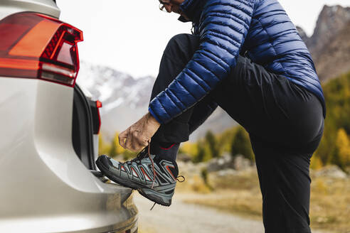 Senior man tying lace of hiking boot at car trunk on vacation - MRAF00761