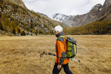 Älterer Rucksacktourist mit Stöcken beim Wandern auf Gras - MRAF00770