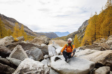 Älterer Wanderer rastet auf einem Felsen in den Rätischen Alpen, Italien - MRAF00786