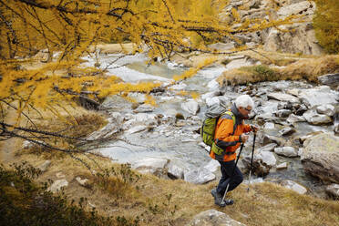 Senior hiker with poles hiking by lake - MRAF00788