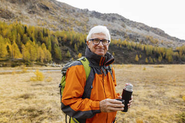 Lächelnder älterer Wanderer mit isoliertem Getränkebehälter in den Rätischen Alpen, Italien - MRAF00793
