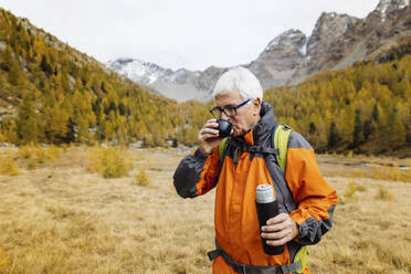 Älterer Wanderer trinkt Kaffee im Gras in den Rätischen Alpen, Italien - MRAF00794