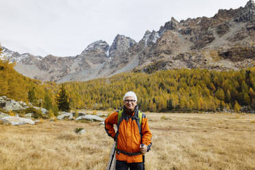 Lächelnder Tourist mit Wanderstöcken inmitten von Gras in den Rätischen Alpen, Italien - MRAF00795