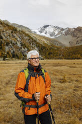 Lächelnder älterer Tourist mit Wanderstöcken, der in die Rätischen Alpen, Italien, blickt - MRAF00798