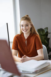 Lächelnde Geschäftsfrau sitzt am Schreibtisch - FKF04559