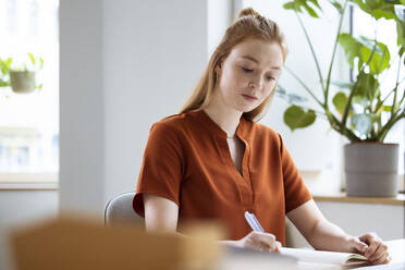 Businesswoman writing in diary at workplace - FKF04560