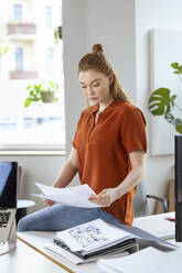Junge Geschäftsfrau prüft Papiere auf dem Schreibtisch - FKF04564