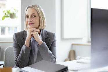 Blond businesswoman with hands on chin at desk - FKF04566