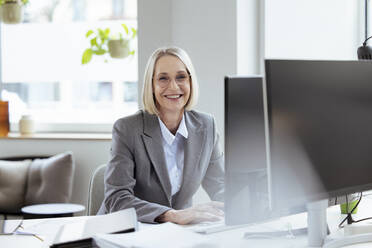 Lächelnde Geschäftsfrau sitzt am Schreibtisch im Büro - FKF04574