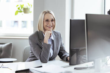 Senior businesswoman with hand on chin using computer in office - FKF04576