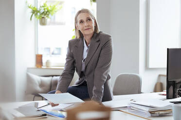 Thoughtful businesswoman with document sitting at desk - FKF04577