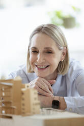 Female architect with hand on chin looking at model in office - FKF04582