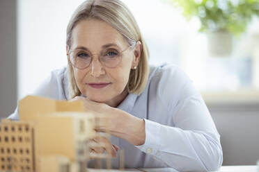 Businesswoman with eyeglasses looking at model in office - FKF04583