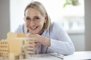 Smiling businesswoman with hand on chin at desk - FKF04584