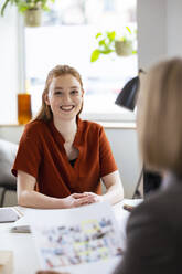Lächelnde Geschäftsfrau am Schreibtisch mit einem Kollegen im Vordergrund - FKF04594