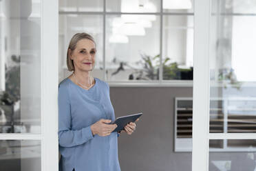Senior businesswoman holding tablet PC at doorway - FKF04613