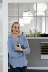 Businesswoman holding tablet PC at office doorway - FKF04615