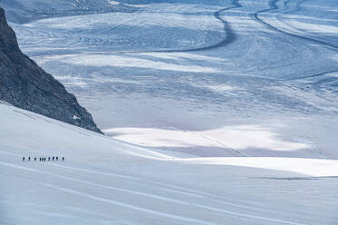 Silhouetten von Wanderern, die durch den schweren Schnee des Aletschgletschers wandern - RUNF04696