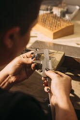 Female craftsperson measuring ring with caliper in workshop - GPF00226