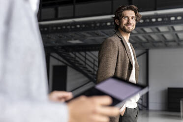 Lächelnder Geschäftsmann, der einen Kollegen mit digitalem Tablet in einer Industriehalle betrachtet - PESF03272
