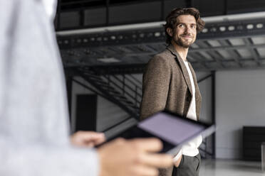 Smiling businessman looking at colleague with digital tablet in industrial hall - PESF03272