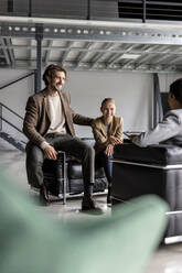 Smiling businessman and colleague sitting on sofa in lobby - PESF03277