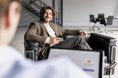 Lächelnder Geschäftsmann schaut auf einen Kollegen, der in der Lobby einen Tablet-PC benutzt - PESF03283