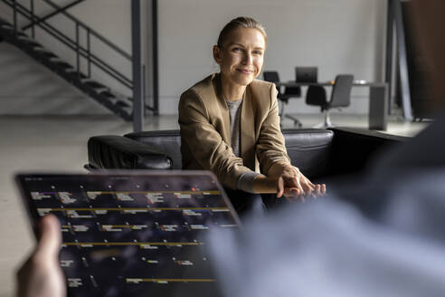 Smiling businesswoman looking at colleague with tablet PC in office - PESF03286