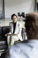 Smiling businesswoman with tablet pc discussing with colleague in lobby - PESF03305