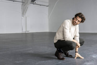 Smiling businessman crouching in industrial hall - PESF03325