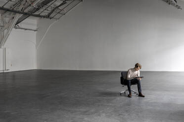 Businessman using tablet pc in empty industrial hall - PESF03343