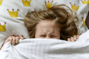 Grimassen schneidendes Mädchen unter der Decke auf dem Bett - EYAF01801