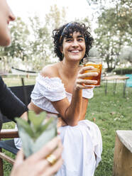 Diverse female friends sitting on chairs in summer park and drinking refreshing cocktail while enjoying summer day together - ADSF31702