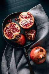 Draufsicht auf einen halbierten und einen ganzen reifen Granatapfel auf einer Bratpfanne, die auf einer zerknitterten Tischdecke auf dem Tisch steht - ADSF31725