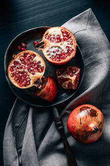 Top view of halved and whole ripe pomegranate on frying pan placed on creased tablecloth on table - ADSF31725