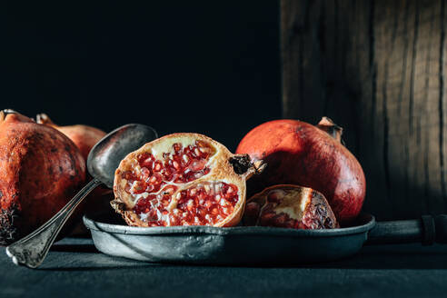 Halbierter und ganzer reifer Granatapfel in der Bratpfanne auf der zerknitterten Tischdecke auf dem Tisch - ADSF31726