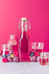 Glasflasche mit frischen Früchten Saft mit reifen Beeren umgeben serviert auf dem Tisch mit Gläsern auf rosa Hintergrund - ADSF31745