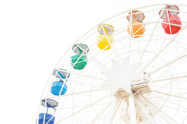 Round public observation wheel with multicolored passenger cabins against clear sky in amusement park - ADSF31758