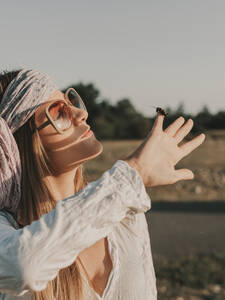 Seitenansicht eines friedlichen weiblichen Hippies mit Sonnenbrille, der sein Gesicht vor der Sonne schützt, während er an einem Sommertag Zeit in der Natur verbringt - ADSF31786
