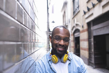 Lächelnder Mann mit Kopfhörern an der Wand lehnend - ASGF01784