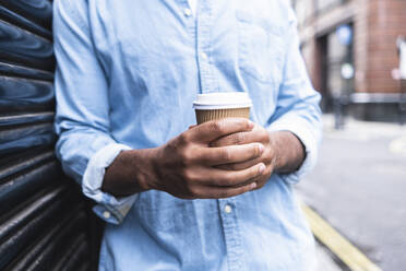 Man holding disposable cup leaning on shutter - ASGF01794