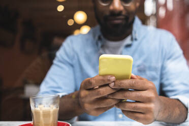 Man using smart phone by coffee glass in cafe - ASGF01802