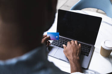 Mann, der in einem Straßencafé eine Online-Zahlung mit Kreditkarte auf seinem Laptop vornimmt - ASGF01806